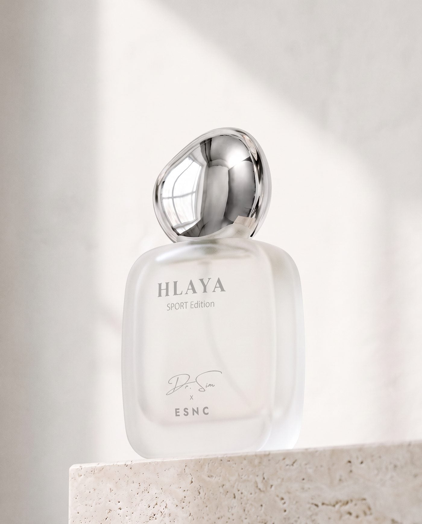 HLAYA turned to the light on a travertine ledge, its chrome pebble cap against a white wall.