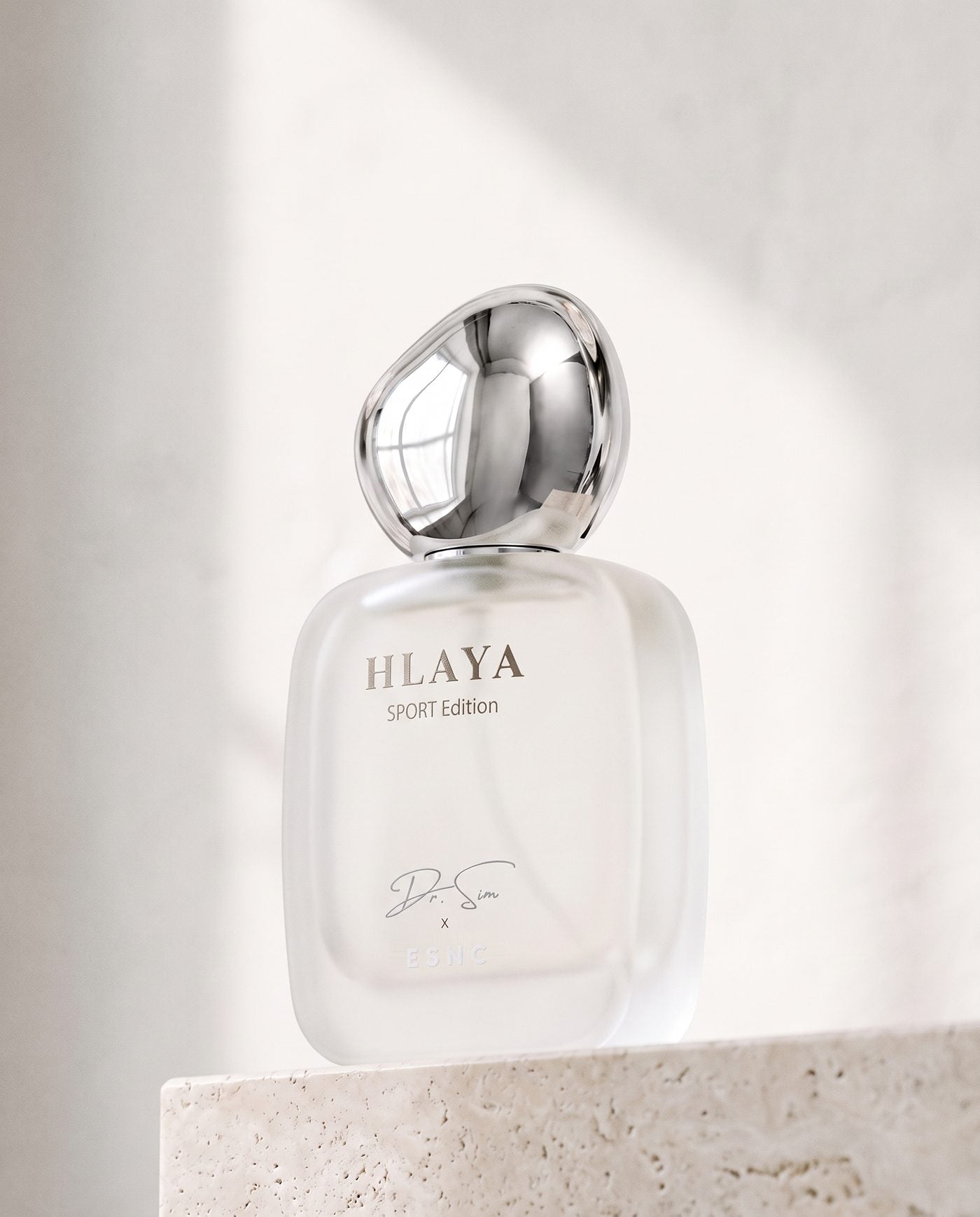 HLAYA turned to the light on a travertine ledge, its chrome pebble cap against a white wall.